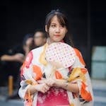 A young woman wearing a colorful floral kimono and holding a fan, embodying traditional Japanese fashion.